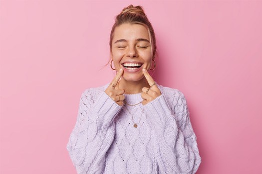 Woman closing eyes pointing to smile with both hands