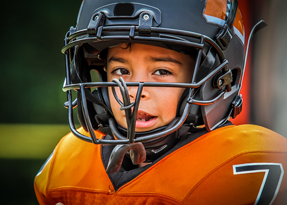 Child in a football uniform with a mouthguard hanging from their helmet