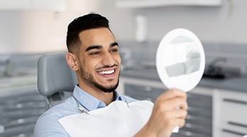 Young man in the dental chair looking at his smile in a mirror