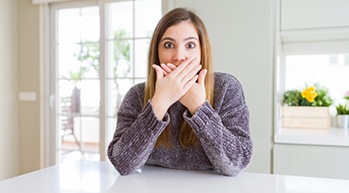 Young woman looking scared and covering her mouth with her hands